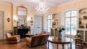 A spacious room with a fireplace, leather armchairs, a round wooden table, and a chandelier. - Private castle with swimming pool in Provence (Lamanon)