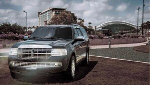 Un SUV de lujo estacionado en un área ajardinada con un edificio moderno al fondo.