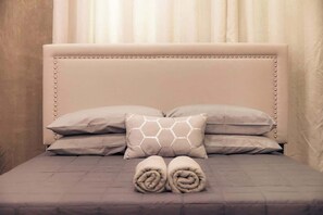 A neatly made bed with a tufted headboard, two pillows, and two rolled towels.