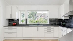 A modern kitchen with white cabinets, a black countertop, and a view of greenery outside. - Great Stay Guest Villa 4 bedrooms (Sandviken)