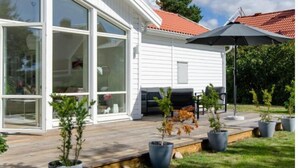 A house with a large sliding glass door, a covered patio with outdoor furniture, and a red-tiled roof. - Great Stay Guest Villa 4 bedrooms (Sandviken)