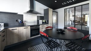 A modern kitchen with a central island, a dining area with a round table and red chairs, and a large window offering a view of the outdoors. - Comfortable villa for 10 with a pool (La Flotte)