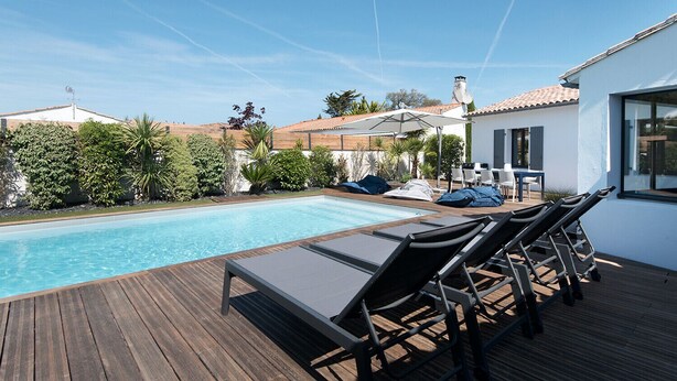 A swimming pool with lounge chairs and umbrellas, surrounded by greenery and a white building with a tiled roof. - Comfortable villa for 10 with a pool (La Flotte)