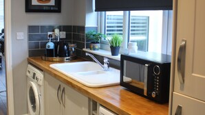 A modern kitchen with a washing machine, a microwave, and a sink. - Spacious 3 bedroom house close to the beach (Lowestoft)