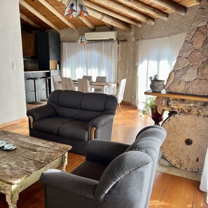 Una sala de estar acogedora con techo de madera, pared de piedra y una mesa de comedor rústica.