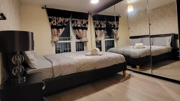 A bedroom with a bed, bedside table, and a large mirror. - Lovely 4 Bedroom Home With Private Parking (Grays)