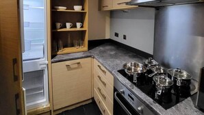 A compact kitchen with a built-in oven, a stainless steel range hood, and a wooden cabinet with shelves. - Lovely 4 Bedroom Home With Private Parking (Grays)