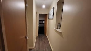A hallway with wooden flooring, beige walls, and a door on the left. - Lovely 4 Bedroom Home With Private Parking (Grays)