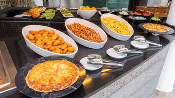 A buffet table with various food items including a pizza, tater tots, and a bowl of French fries.