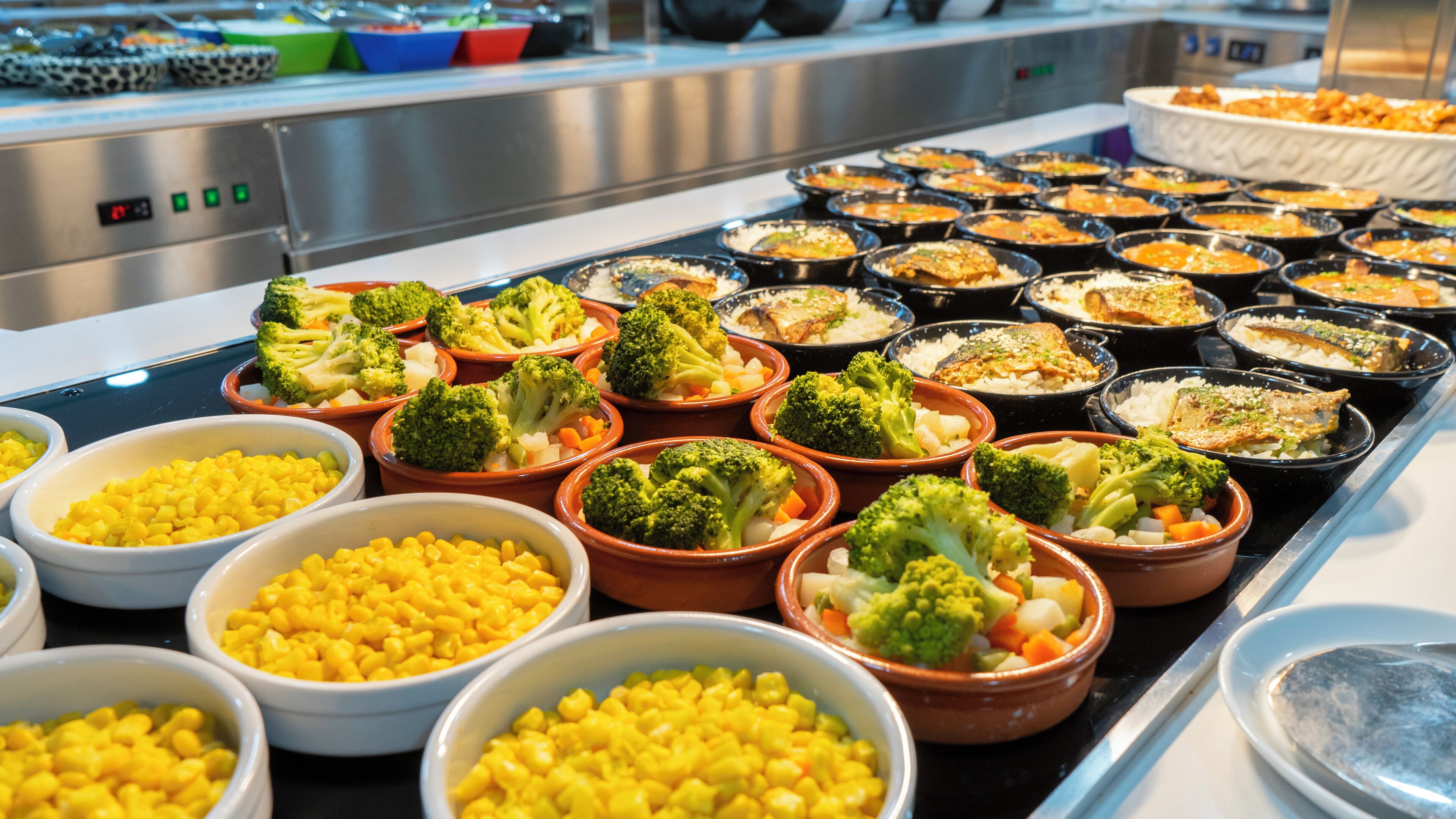 Een buffet met diverse gerechten, waaronder broccoli, mais en rijst.