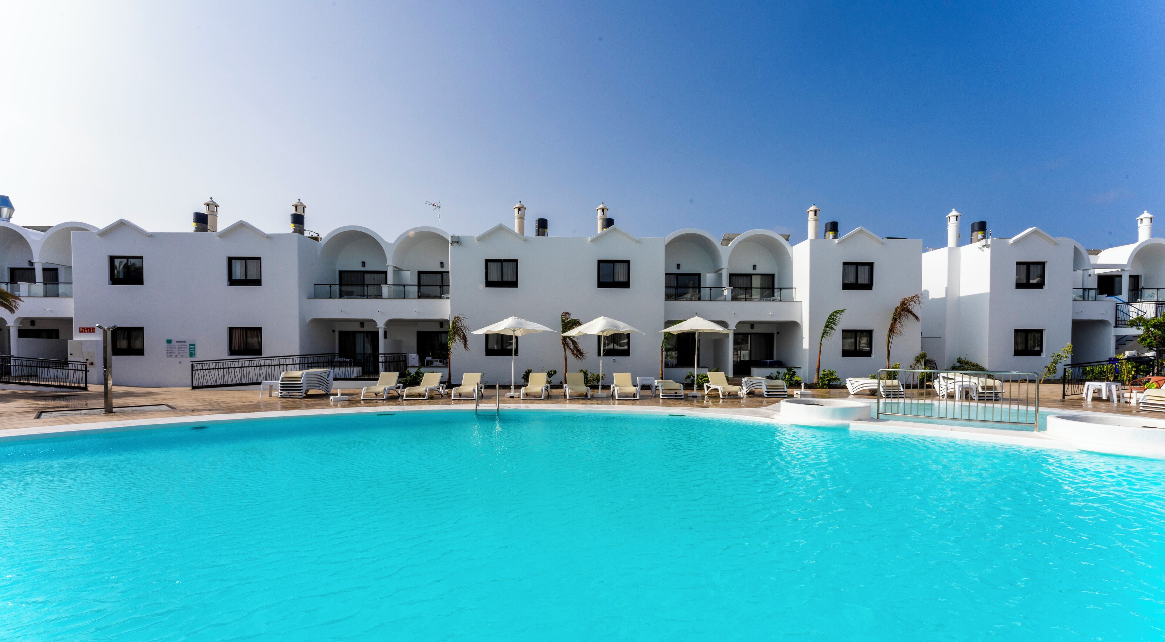 A hotel with a swimming pool, white architecture, and multiple balconies.
