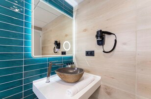 Un baño moderno con un lavamanos de piedra, un espejo grande y un secador de pelo montado en la pared.
