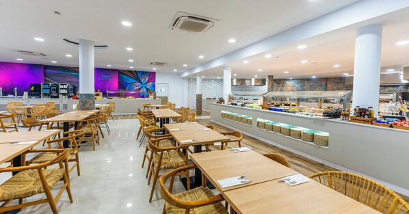 A modern restaurant with wooden tables and chairs, a counter with food displays, and a colorful mural on the wall.