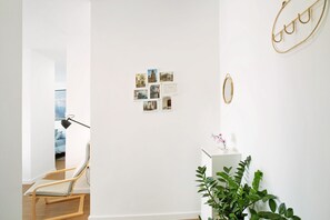 Um quarto com uma cadeira de madeira, uma escrivaninha com uma planta e uma parede com fotografias e um anel dourado.