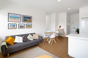 Uma sala de estar moderna com um sofá cinza, cadeiras brancas, uma mesa de jantar de madeira e quadros nas paredes.