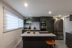 A modern kitchen with a central island, built-in appliances, and a window with blinds. - Villa 'Baraka' with Private Pool, Wi-Fi and Air Conditioning (SALON DE PROVENCE)