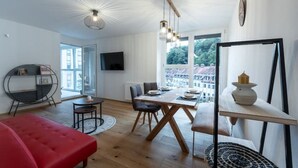 Ein modernes Wohnzimmer mit Essbereich, einem roten Sofa, einem runden Tisch und einem an der Wand montierten Fernseher.
