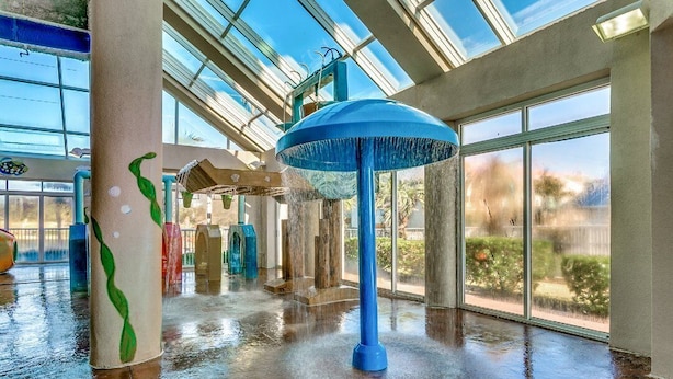 Un vaste espace intérieur agrémenté d’un élément aquatique au centre, de grandes fenêtres et d’un sol mouillé.