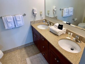 Ein Badezimmer mit zwei Waschbecken, einem großen Spiegel und einem Handtuchhalter mit gefalteten Handtüchern.