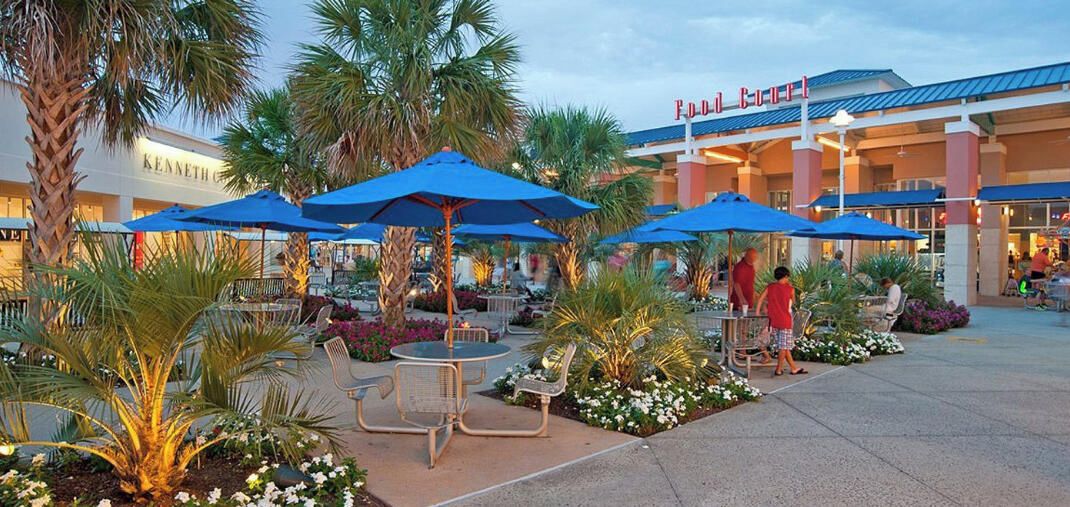 An outdoor dining area with umbrellas and chairs, a Kenneth Cole store in the background, and a pedestrian walkway.