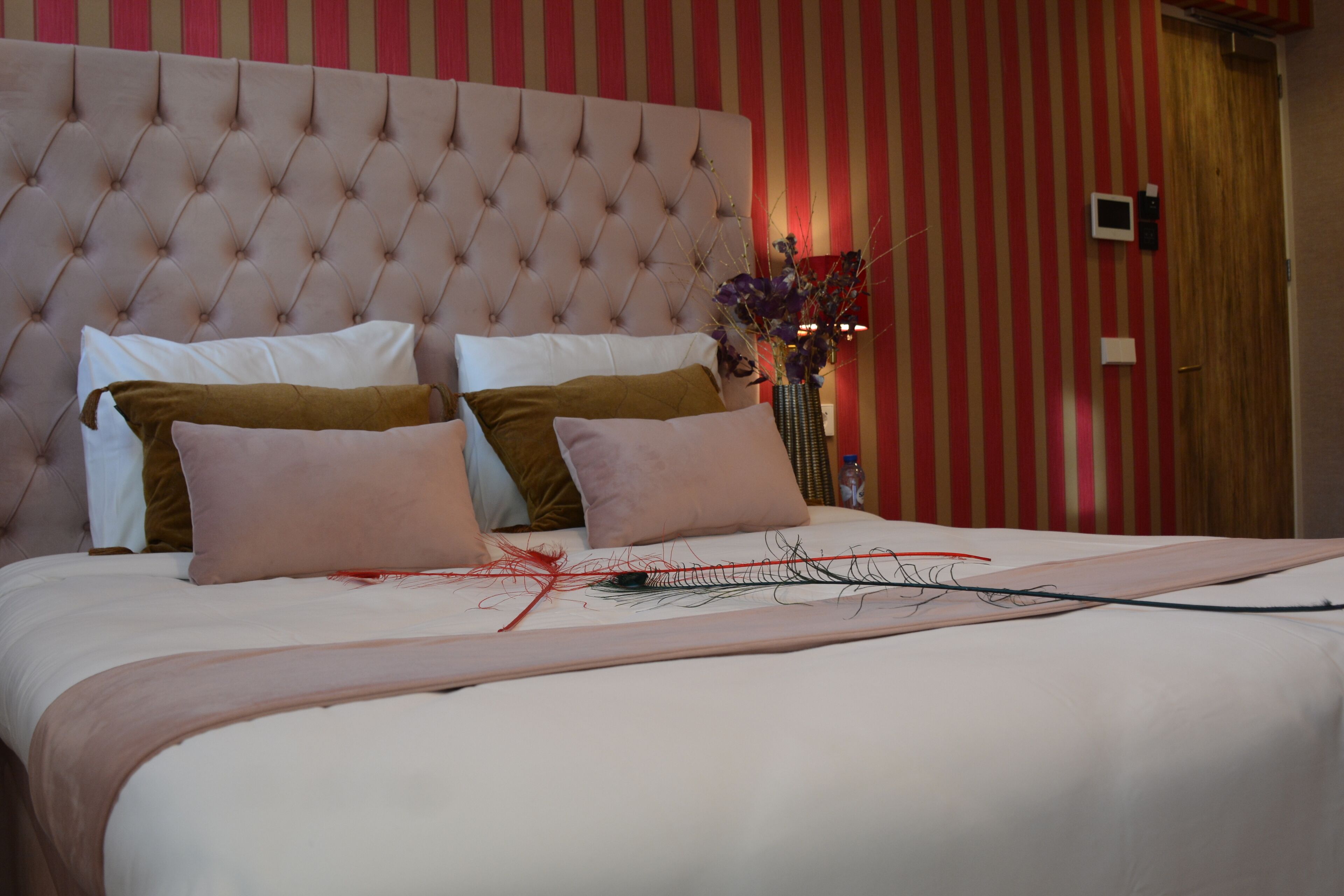A neatly made bed with a tufted headboard, a vase with flowers, and a striped wall in the background.