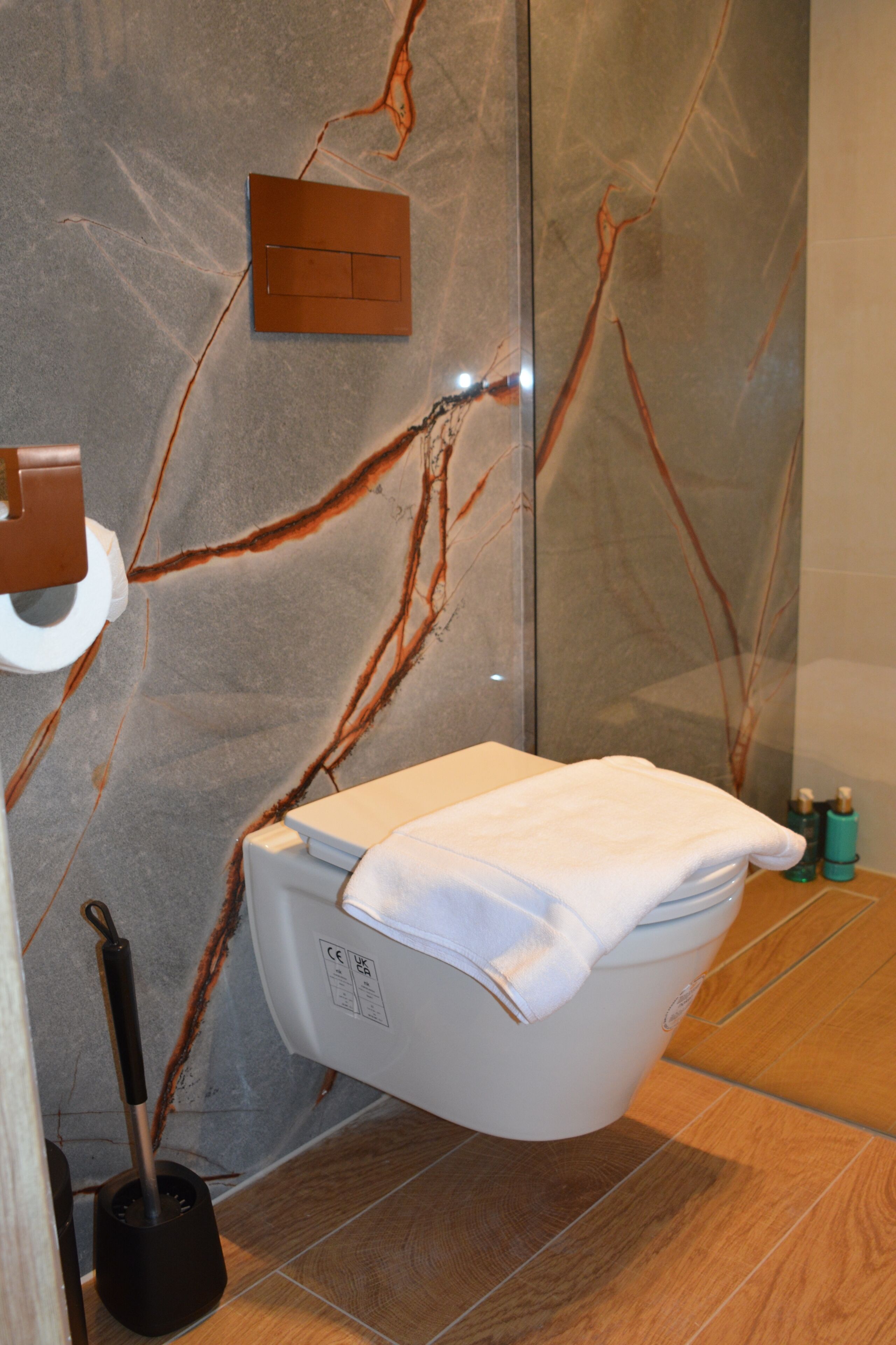 A modern bathroom with a marble wall, a toilet, a hand dryer, and a broom.