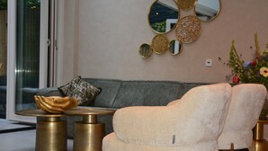 A modern living room with a grey sofa, two armchairs, a round coffee table, and a decorative mirror on the wall. - If boutique hotel (Amsterdam)