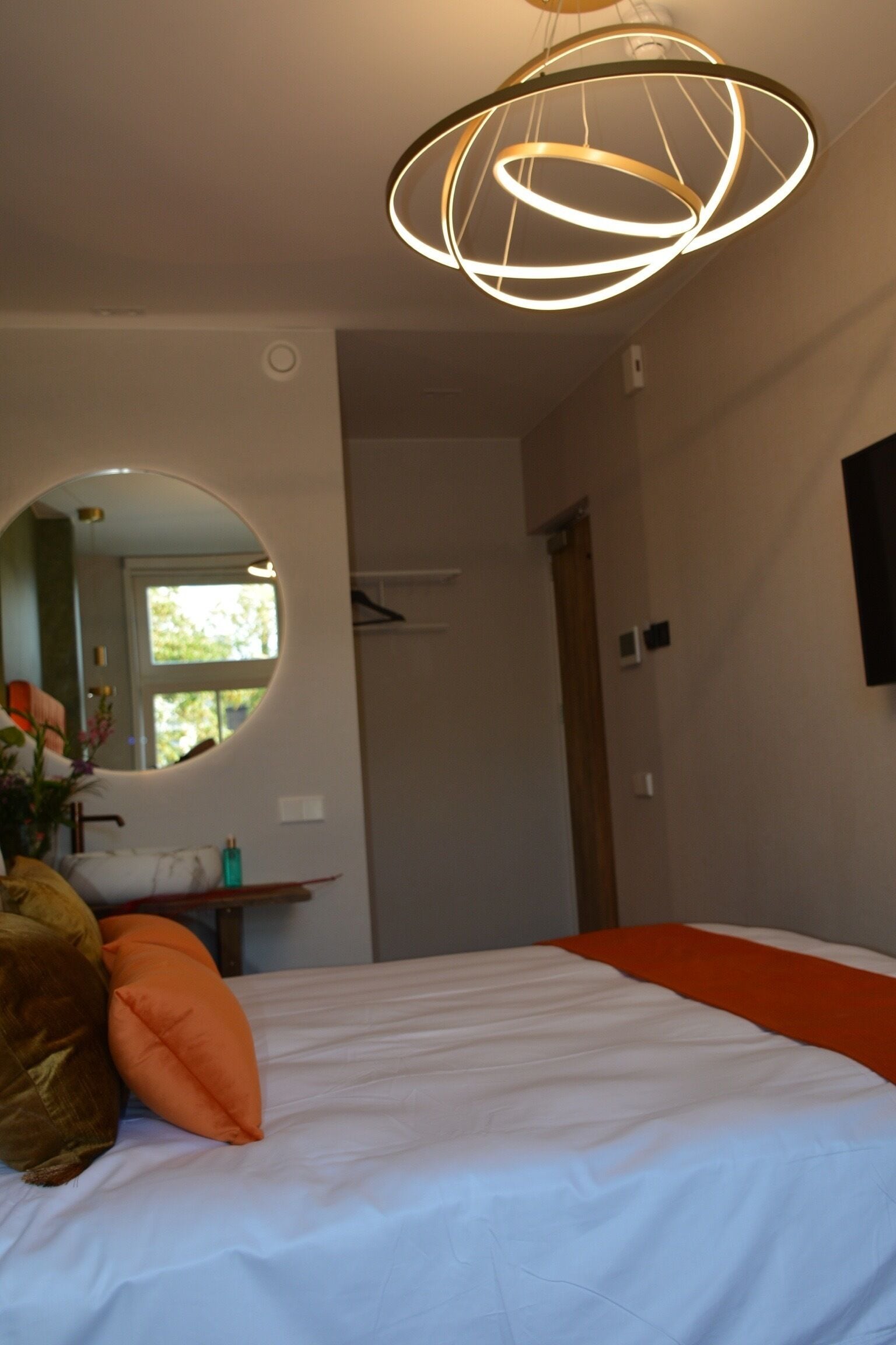 A bedroom with a bed, a round mirror, and a modern light fixture.