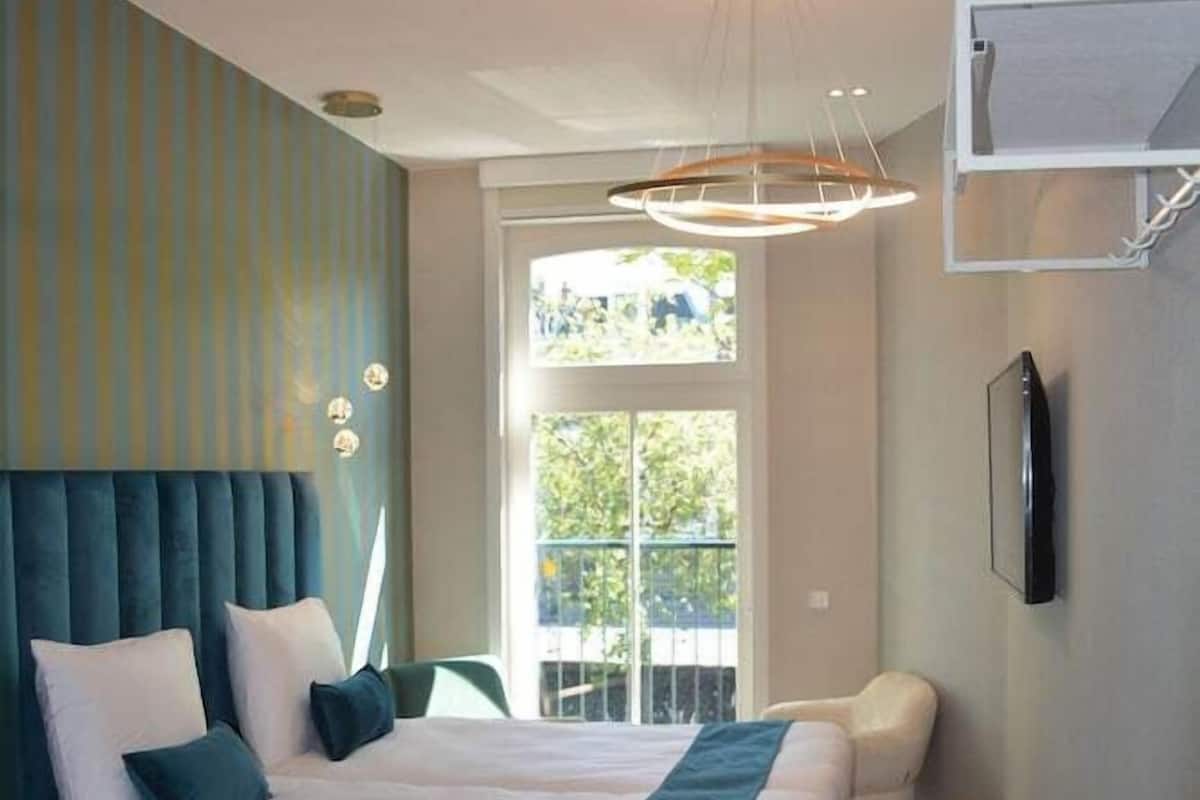 A bedroom with a bed, a chair, a TV, and a window.