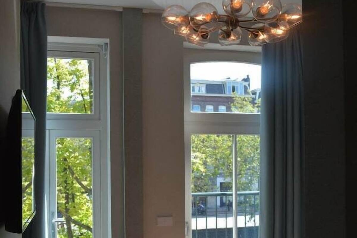 A bedroom with a bed, a chair, a hanging light fixture, and large windows.