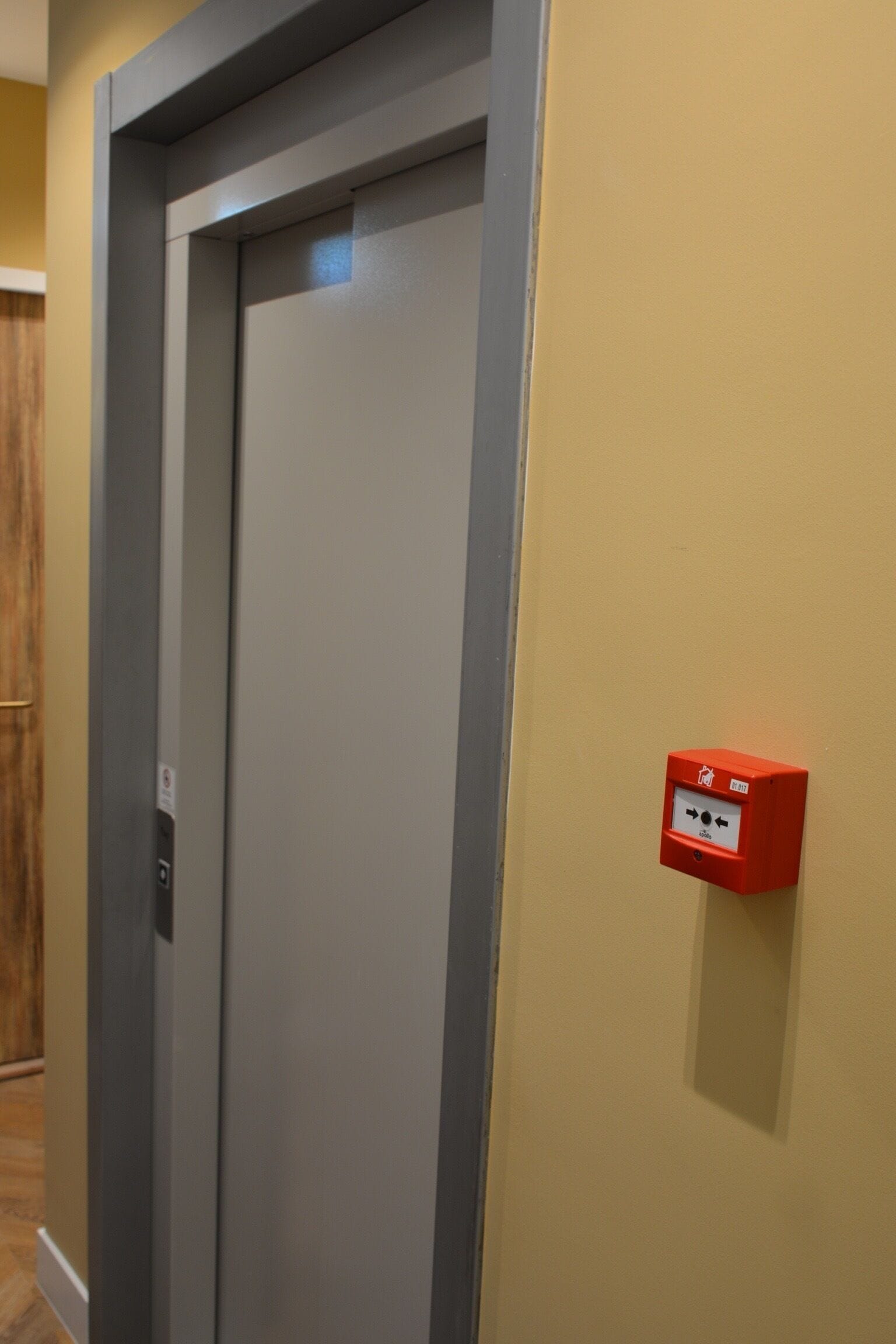A door with a grey frame and a red emergency pull station on the wall.