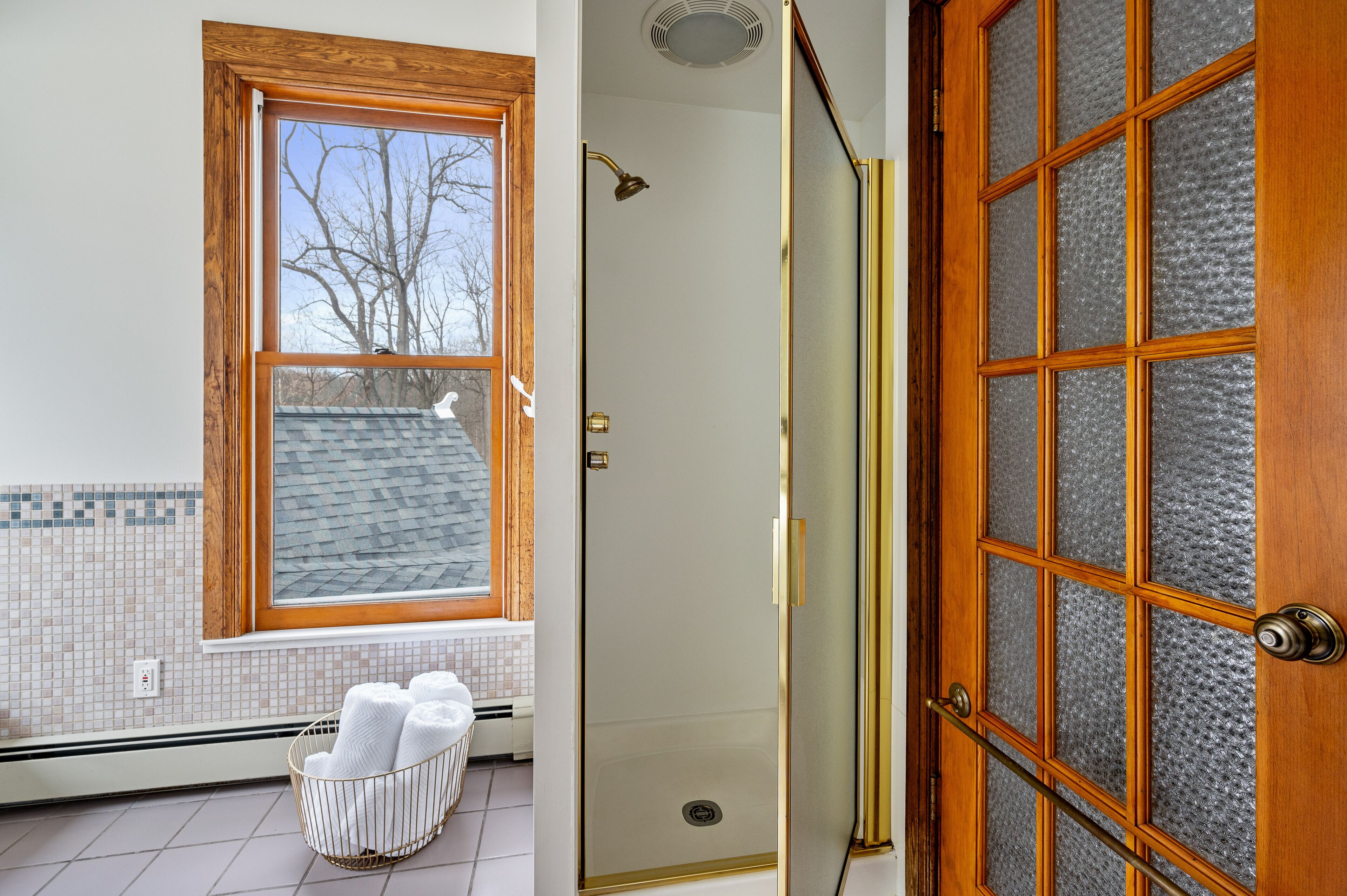 Un baño con ventana, ducha y puerta con paneles de vidrio esmerilado.
