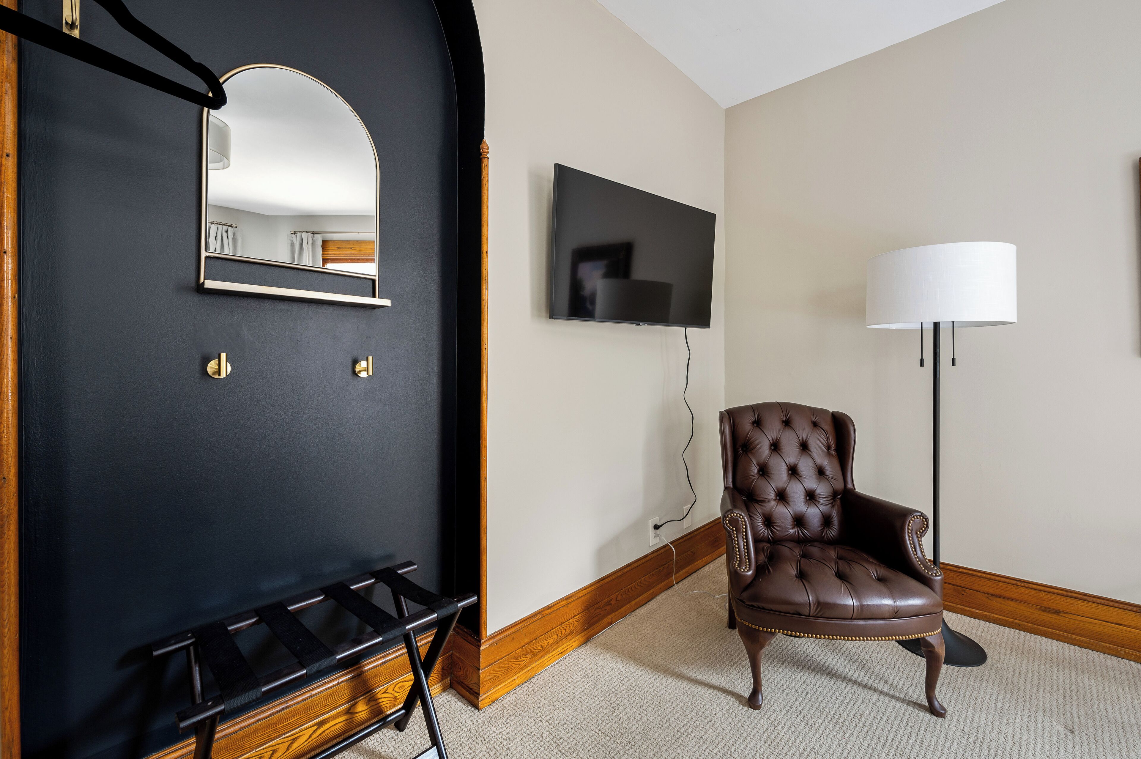 Una habitación con una puerta negra, un espejo, un televisor de pantalla plana, un sillón de cuero y una lámpara de pie.