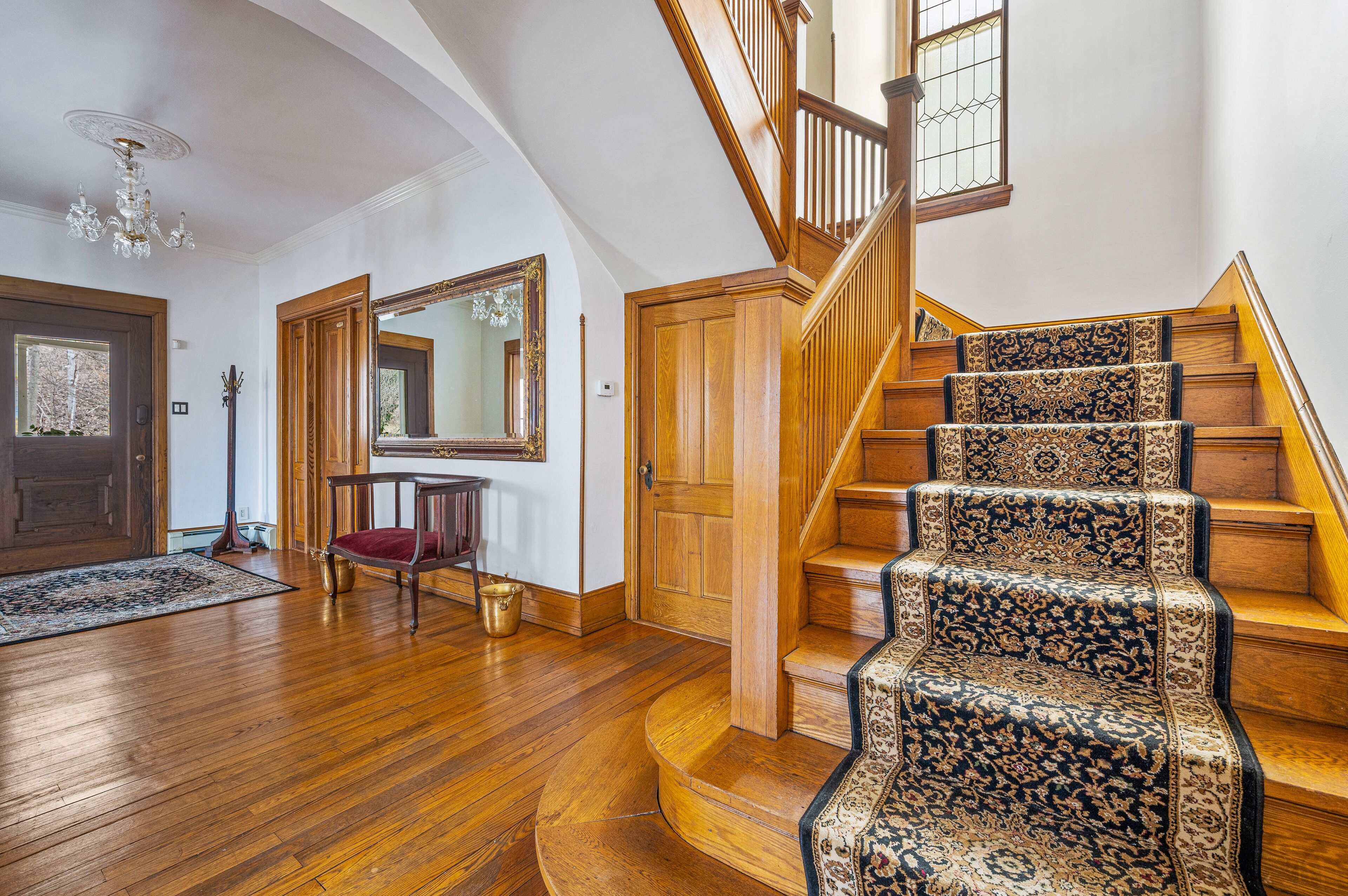 A grand staircase with ornate carpeted steps, a chandelier, and a wooden door.