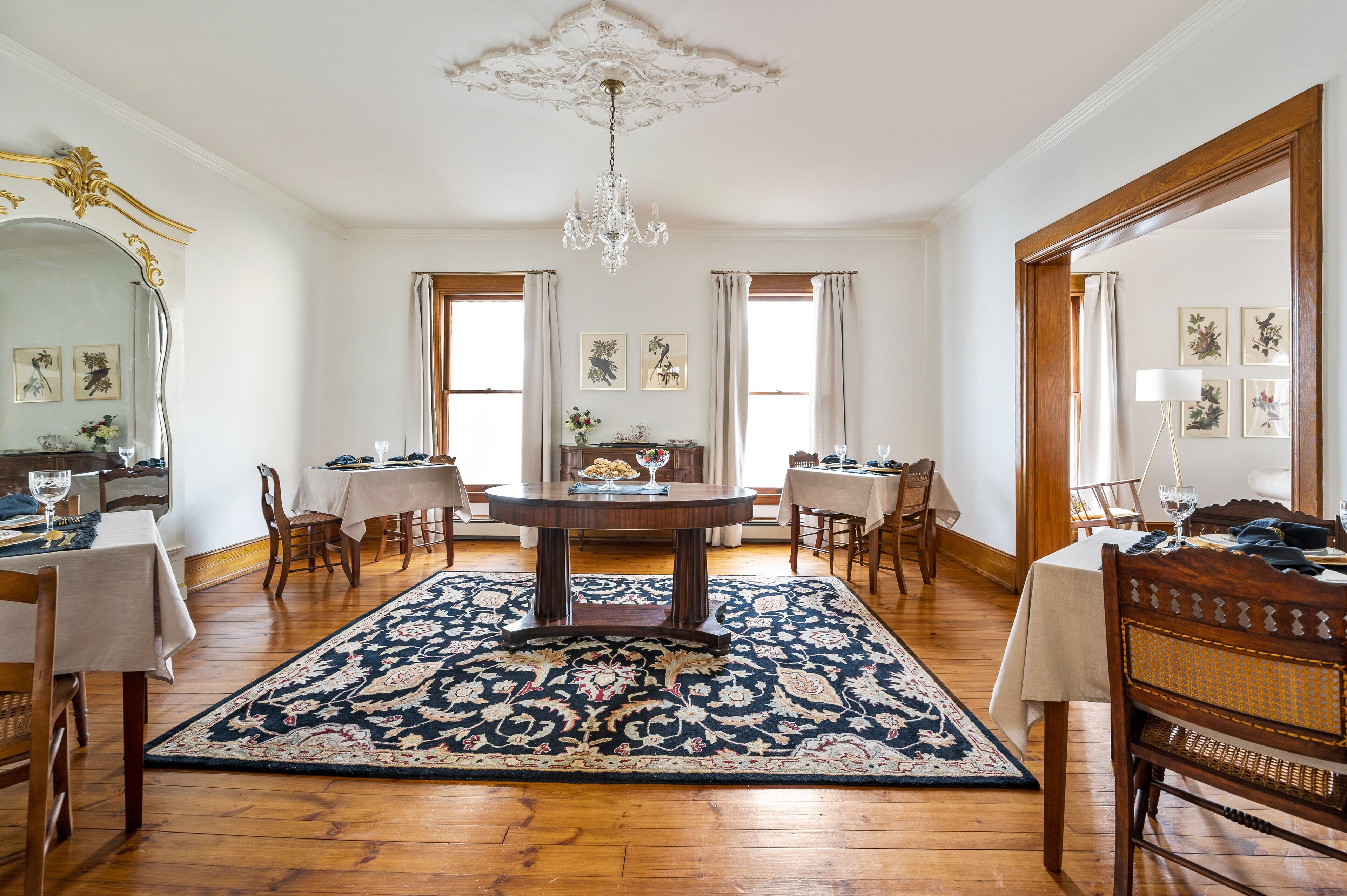 Une salle à manger avec une table ronde, des chaises, un lustre et un grand miroir.
