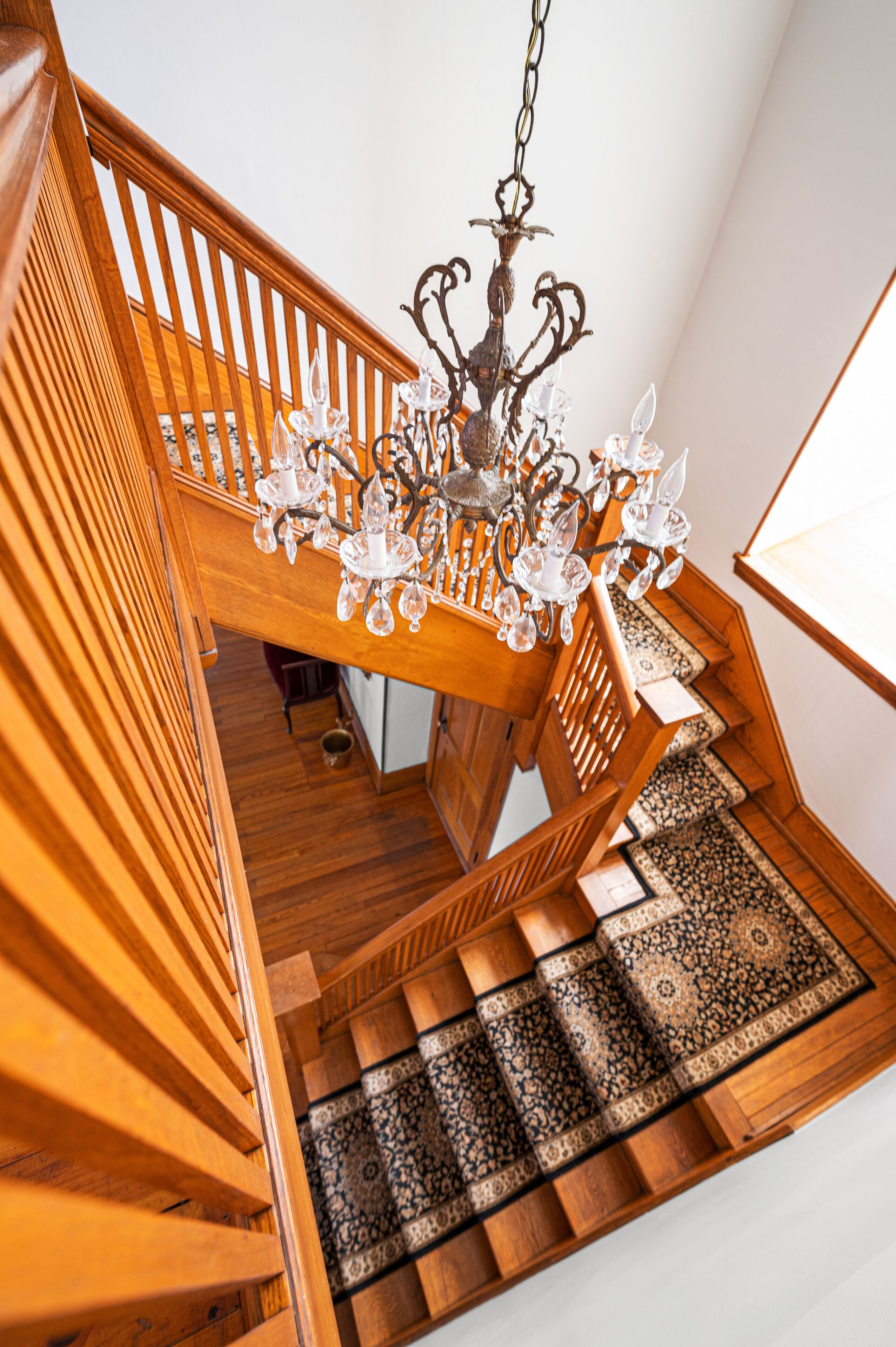 A wooden staircase with a chandelier and patterned carpet.