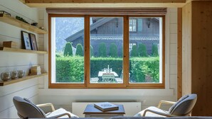 Um quarto aconchegante com uma janela grande, um sofá, duas cadeiras, uma mesa pequena e prateleiras de madeira.