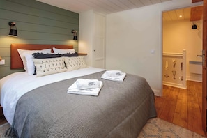 Een netjes opgemaakt bed met een bedovertrek met patroon en kussens, een nachtkastje met een lamp, en een deur naar een badkamer met een handdoekhouder.