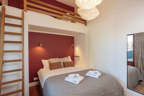 Habitación de hotel con literas, un edredón estampado, dos almohadas, una lámpara de noche y un espejo.
