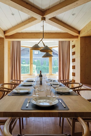 Een eetgedeelte met een houten tafel, gedekt voor een maaltijd, grote ramen en uitzicht op groen.