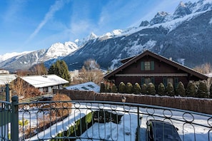 Een chalet met een met sneeuw bedekte dak, een stenen muur en een uitzicht op besneeuwde bergen.