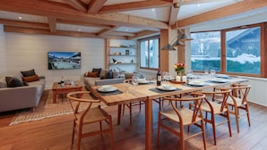 Uma sala de estar espaçosa com uma mesa de jantar de madeira, assentos confortáveis e uma janela grande com vista para a paisagem nevada.