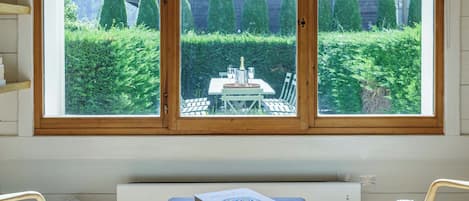 Une pièce dotée d’une grande fenêtre donnant sur un bâtiment en bois et un jardin bien entretenu.