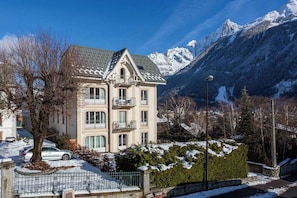 Un immeuble à plusieurs étages doté d’un balcon, entouré d’un paysage enneigé et de montagnes.