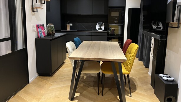 Une cuisine moderne avec des meubles de rangement noirs, une table à manger en bois et des chaises colorées.