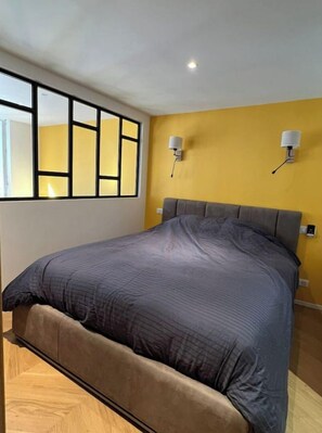 A bedroom with a bed, a window with blinds, and two wall-mounted lamps.
