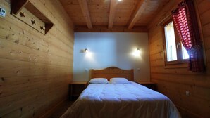 Una habitación de cabaña de madera con cama, dos lámparas fijadas a la pared y una ventana con cortina roja.