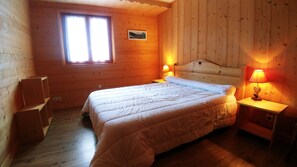 Une pièce chaleureuse aux murs en bois, avec un lit, deux lampes de chevet, une fenêtre et un petit tableau accroché au mur.