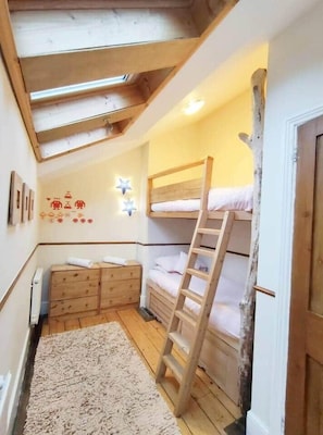A room with a bunk bed, wooden dresser, and a ladder.