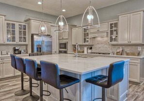 A modern kitchen with a central island, bar stools, stainless steel appliances, and pendant lighting. - Ocean View * 5BR Luxury Single Family House! (Ocean View)